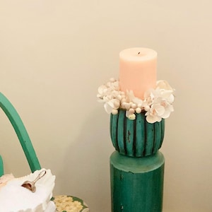 May include: A white ceramic mug with a black handle and the text "But First, Coffee" in a bold, black font. The mug is set against a blurred background, suggesting a cozy setting.