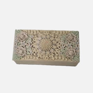 Könnte beinhalten: Eine rechteckige, beige dekorative Box mit floralem Design. Die Box zeigt geschnitzte Rosen, Blätter und ein zentrales Blumenmuster. Die Blumen sind in Beige-, Hellgrün- und Rosatönen gehalten.