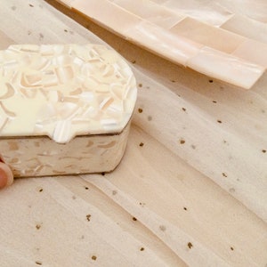 May include: A small, oval-shaped trinket box with a white, pearlescent finish. The box is decorated with a swirling pattern of white and cream-coloured pieces.
