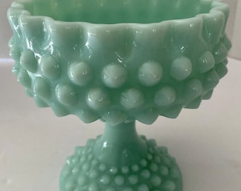 Op de afbeelding: Een vintage, lichtgroene glazen voetkom met een getextureerd, geperld oppervlak. De kom heeft een brede, ronde bovenkant en een hoge, slanke voet.