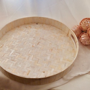 May include: A round, white woven tray with two handles. The tray is made of natural materials and has a woven pattern.
