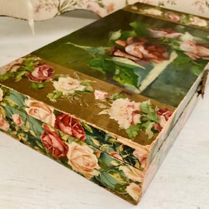 May include: A vintage wooden box with a floral design. The box is decorated with a gold trim and a floral pattern. The lid of the box features a painting of roses.