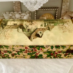 May include: A vintage wooden box with a hinged lid. The box is covered in a green and white paper with a holly pattern. The top of the box features a printed image of a snowy house with a tree in the foreground.