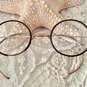 May include: Round, brown-framed glasses with gold metal arms and a delicate, white lace background.