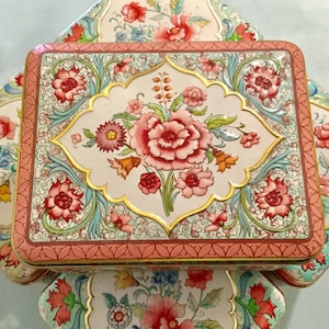 Peut inclure: Un ensemble de trois boîtes en étain vintage avec des motifs floraux. Les boîtes sont empilées les unes sur les autres et présentent des motifs complexes dans des tons de rose, bleu et vert.