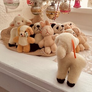 Puede incluir: Un grupo de peluches, incluyendo un cordero, un conejito, un oso y un panda, est&aacute;n dispuestos sobre una superficie de arpillera marr&oacute;n. Los peluches son todos blancos con ojos y narices negros.
