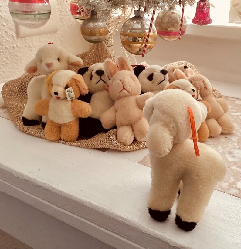 Puede incluir: Un grupo de peluches, incluyendo un cordero, un conejito, un oso y un panda, est&aacute;n dispuestos sobre una superficie de arpillera marr&oacute;n. Los peluches son todos blancos con ojos y narices negros.