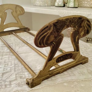 May include: An antique brass book stand with an Art Nouveau design. The stand features two decorative end pieces with curved, organic shapes and three horizontal bars to hold books. The brass has a warm, aged patina.