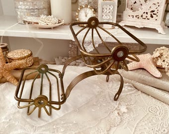 Puede incluir: Un jabonera antigua de latón con un diseño de doble compartimento. La jabonera presenta un asa curvada y un diseño calado decorativo. El metal tiene una pátina vintage, lo que aumenta su encanto. El plato está diseñado para contener jabón y otros elementos esenciales del baño.
