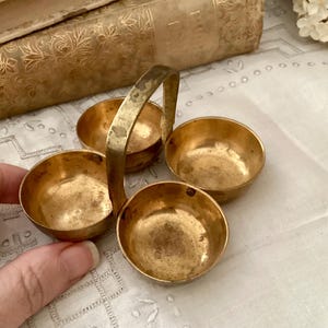 May include: A vintage brass condiment server with four small bowls and a handle. The server has a tarnished, aged appearance, suggesting it is an antique. The bowls are round and appear to be empty.