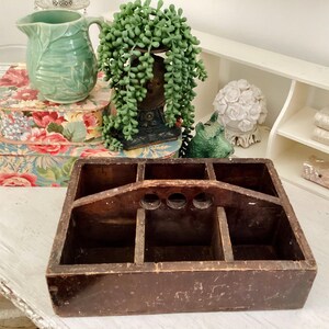 May include: A dark brown wooden tool caddy with a handle and multiple compartments. The caddy is empty and sitting on a white surface.