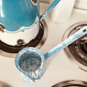 May include: A blue and white enamel pitcher and a blue and white enamel ladle on a white stovetop.