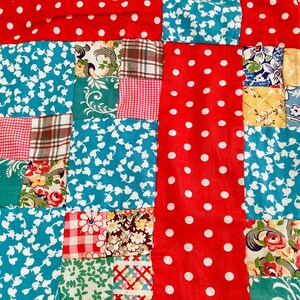 May include: A patchwork quilt featuring a variety of fabric squares in red, white, and turquoise. The design includes patterns such as white polka dots on red, floral prints, red and white gingham checks, and brown plaid, all stitched together.