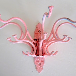 May include: A pink metal coat rack with multiple hooks. The rack has a decorative design at the bottom.