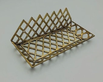 May include: A gold-colored, geometric tray with a diamond lattice design. The tray has a triangular shape with a raised back, suitable for holding small items. The openwork pattern allows for visibility and adds a decorative element.