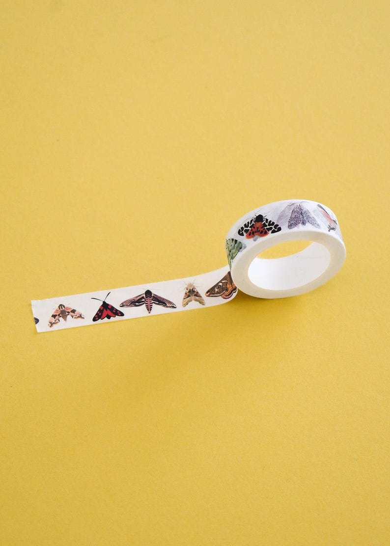 May include: A roll of white washi tape featuring a repeating pattern of various moth species in shades of brown, black, red, and green. The tape is partially unrolled, displaying detailed illustrations of different insects along its length.