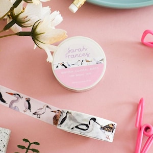 May include: A roll of white washi tape featuring watercolor illustrations of various coastal birds. The label on the roll reads Sarah Frances, British Coastal Birds, 10m Washi Tape. The tape pattern displays birds including a puffin and a heron.