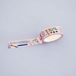May include: A roll of light pink washi tape featuring a repeating pattern of art supplies including paintbrushes, pens, and a watercolor palette. The text "I AM AN ARTIST" is printed in a colorful font along the tape, which is partially unrolled.