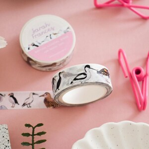 May include: A roll of decorative washi tape featuring watercolor illustrations of various coastal birds, including a puffin and an avocet. The tape is white with a repeating pattern of birds in black, white, and brown tones. The label reads Sarah Frances.