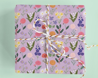 Può includere: Un regalo avvolto con un motivo floreale su carta lavanda. Il design presenta vari fiori nei toni del rosa, giallo, viola e bianco. Il regalo è legato con un fiocco di spago bianco e oro, creando una presentazione decorativa.