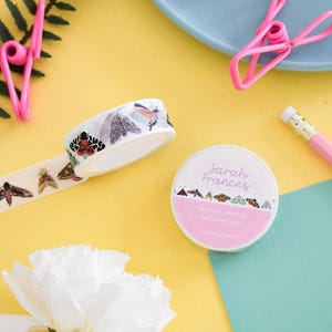 May include: Two rolls of white washi tape featuring colorful illustrations of various moth species. One roll is upright, showing the label with the text Sarah Frances and British Moths, while the other roll is tilted, displaying the moth pattern.
