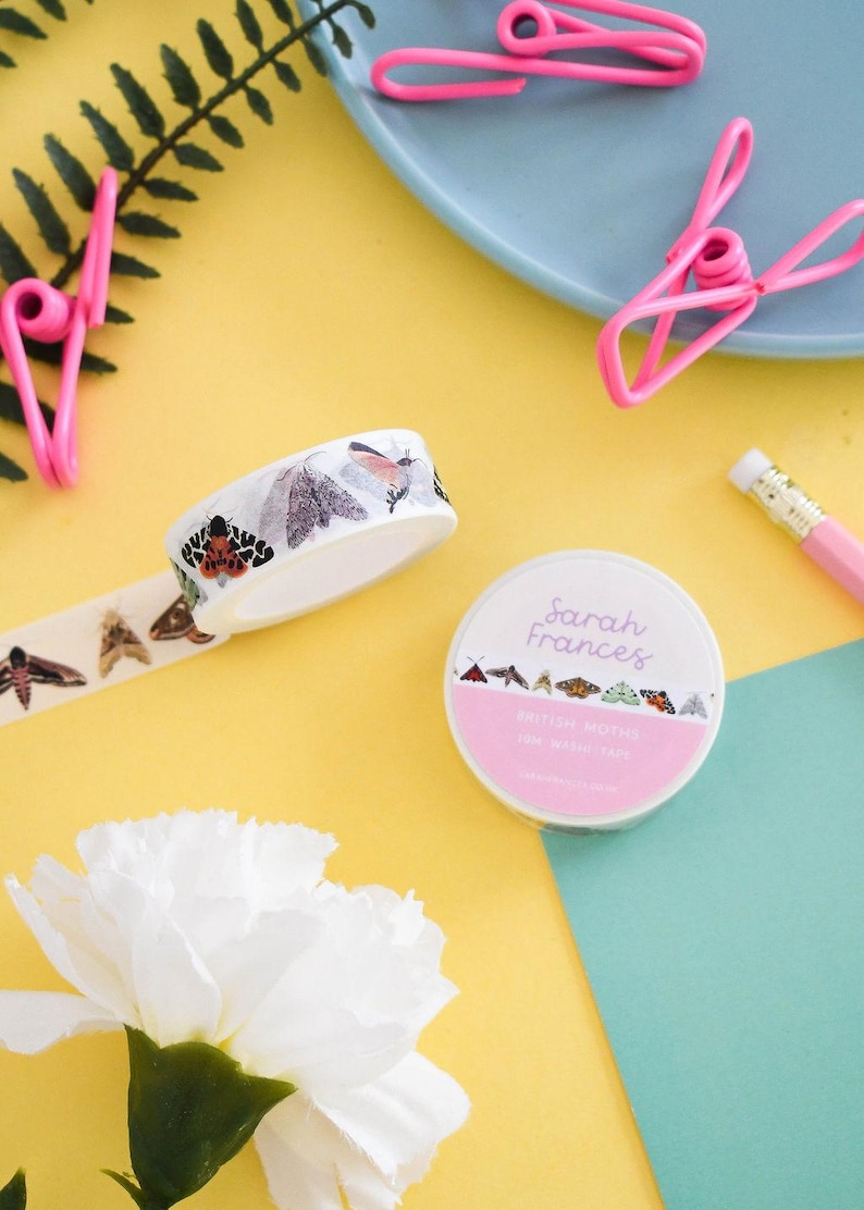 May include: Two rolls of white washi tape featuring colorful illustrations of various moth species. One roll is upright, showing the label with the text Sarah Frances and British Moths, while the other roll is tilted, displaying the moth pattern.
