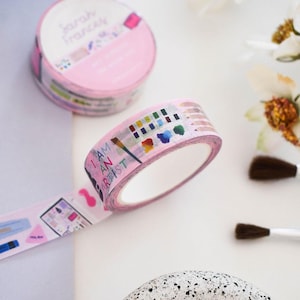 May include: Two rolls of light pink washi tape featuring artistic illustrations of paintbrushes, watercolor palettes, and colored pencils. The tape displays the text I AM AN ARTIST in colorful letters, along with various art supply graphics.