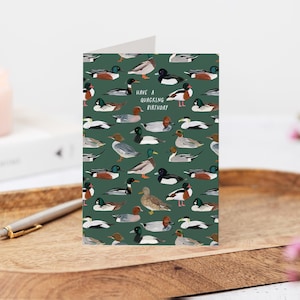May include: A birthday card featuring a pattern of ducks in various poses against a dark green background. The card includes the text "Have a quacking birthday". The ducks are depicted in shades of brown, white, black, and green.