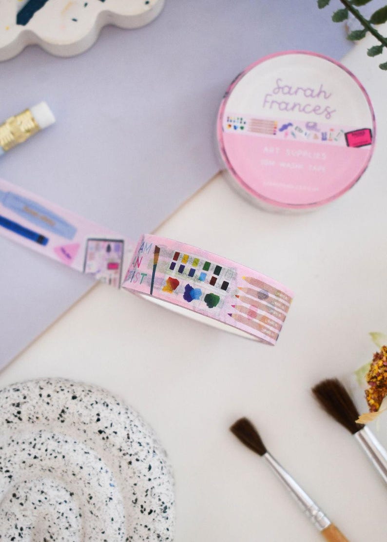 May include: A roll of pink washi tape featuring illustrations of art supplies including paint palettes, colored pencils, and brushes, with the text Sarah Frances and Art Supplies on the packaging and the phrase I am an artist on the tape.