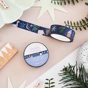 May include: A roll of dark blue washi tape featuring a Christmas bird pattern, labeled Sarah Frances Christmas Birds 10m Washi Tape. The tape displays illustrations of birds in winter attire, snowflakes, and holly against a dark blue background.