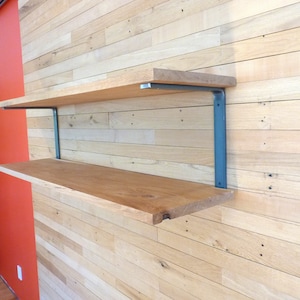 May include: Two wooden shelves with metal brackets mounted on a light wood wall. The shelves are made of natural wood with a rustic finish. The brackets are a dark gray color.