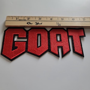 May include: Red embroidered patch with the word "GOAT" in black outlined letters.