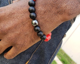 May include: A bracelet with black and red beads. The bracelet has a silver metal bead in the center.