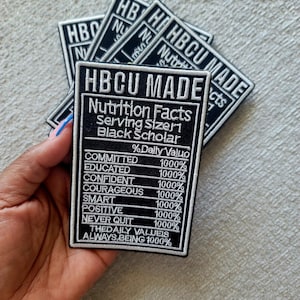 May include: Black and white embroidered patch with the text "HBCU MADE" and "Nutrition Facts". The patch lists positive attributes such as "Committed", "Educated", and "Confident", each with a 1000% value.