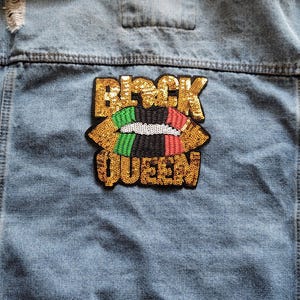 May include: A denim jacket with a gold sequined patch that says "Black Queen" with a red, black, green, and yellow lip design.