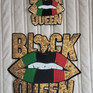 May include: Two sequined patches with the words "BLACK QUEEN". The top patch is smaller. The lips are colored with green, black, and red sequins. The letters are gold.