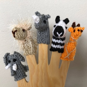 May include: Five finger puppets made of knitted fabric, each depicting a different animal: a rhino, a zebra, a giraffe, a llama, and an elephant. The puppets are displayed on a wooden hand.