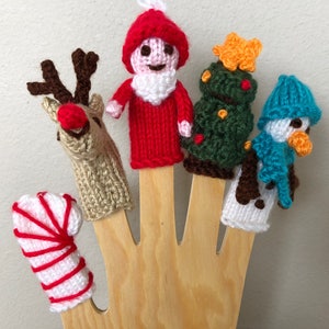 May include: Five knitted finger puppets on a wooden hand. The puppets are a red and white candy cane, a brown reindeer, a red Santa Claus, a green Christmas tree, and a blue and white snowman.