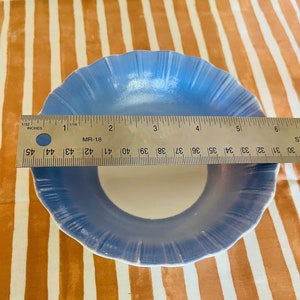 May include: A light blue ceramic bowl with a white interior and a scalloped edge. The bowl is 5 inches in diameter.