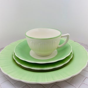 May include: A set of three green and white ceramic plates with a scalloped edge. The plates are stacked with a white teacup with a green rim on top.