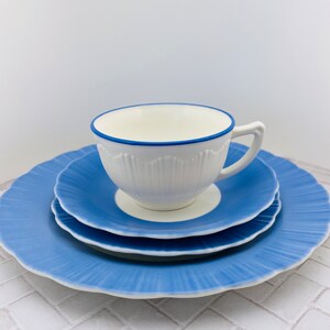May include: A white teacup with a blue rim and a blue and white saucer. The saucer is on top of a larger blue saucer.