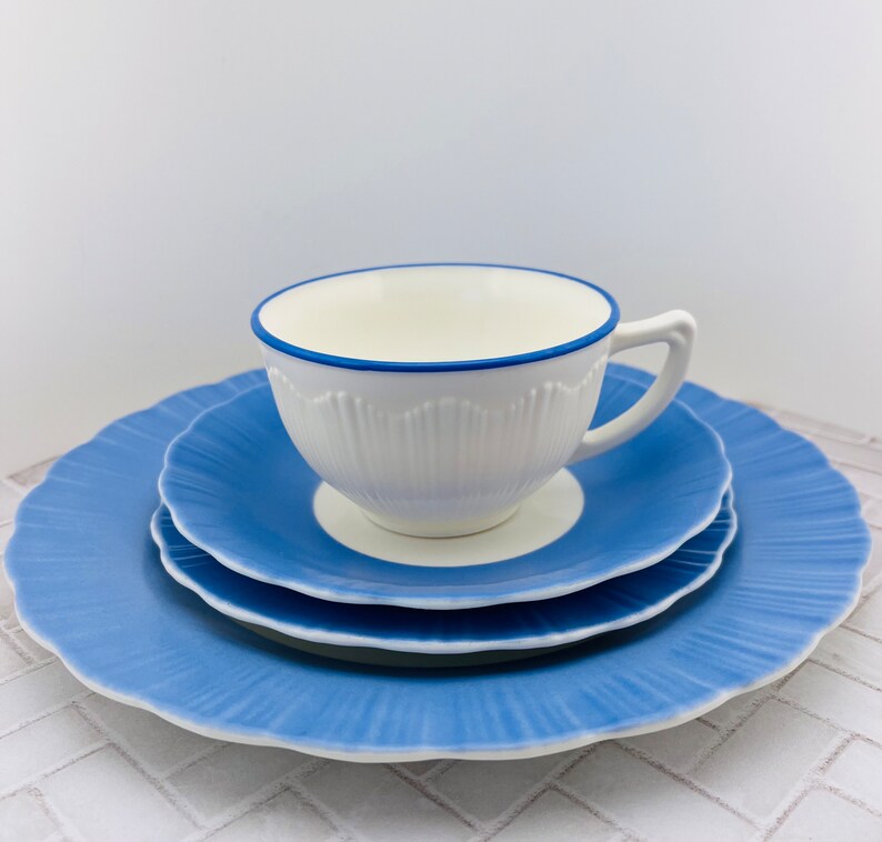May include: A white teacup with a blue rim and a blue and white saucer. The saucer is on top of a larger blue saucer.