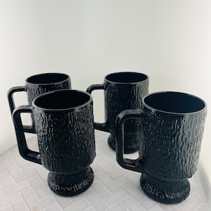 May include: Set of four black glass mugs with a textured, wood-like design. The mugs have a wide base and a handle.