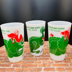May include: Three white ceramic mugs with green and red illustrations. The mugs feature a green dinosaur, a green triceratops, and a red creature with a green hat. Each mug has the text "Other Bay State and Her Friends" printed on it.