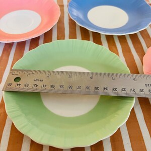 May include: Four vintage teacups with scalloped edges. The cups are white with a single band of color around the rim. The colors are pink, blue, green, and a fourth cup that is out of focus.