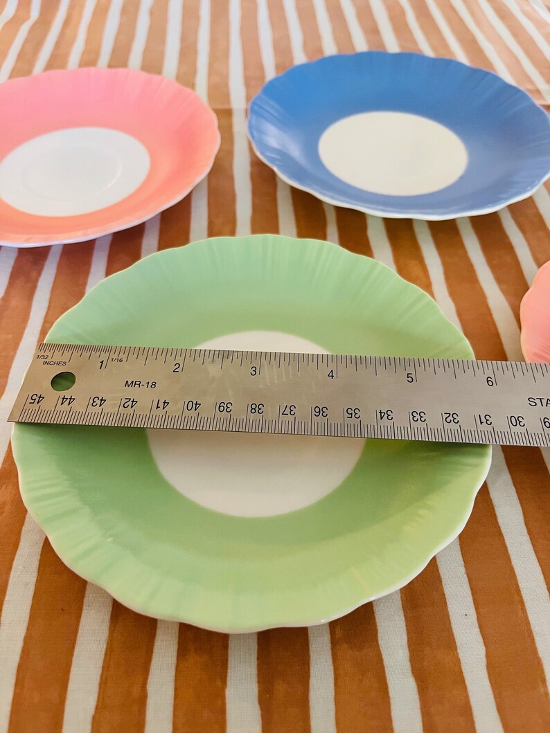 May include: Four vintage teacups with scalloped edges. The cups are white with a single band of color around the rim. The colors are pink, blue, green, and a fourth cup that is out of focus.