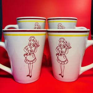 May include: Set of four white ceramic mugs with a yellow and maroon band around the top. Each mug features a cartoon image of a woman in a red dress and white apron holding a tray with food.