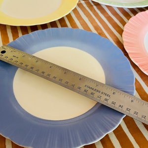 May include: A set of four pastel-colored ceramic plates with scalloped edges. The plates are yellow, green, pink, and blue. A ruler is placed on top of the blue plate, measuring 7 inches.