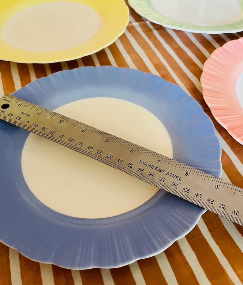 May include: A set of four pastel-colored ceramic plates with scalloped edges. The plates are yellow, green, pink, and blue. A ruler is placed on top of the blue plate, measuring 7 inches.