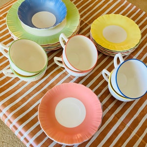 May include: A set of vintage teacups and saucers in various pastel colors, including pink, yellow, blue, and green. The cups and saucers have a scalloped edge and a delicate floral design.
